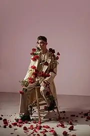 Photograph of a model sitting on a chair with his body full of roses